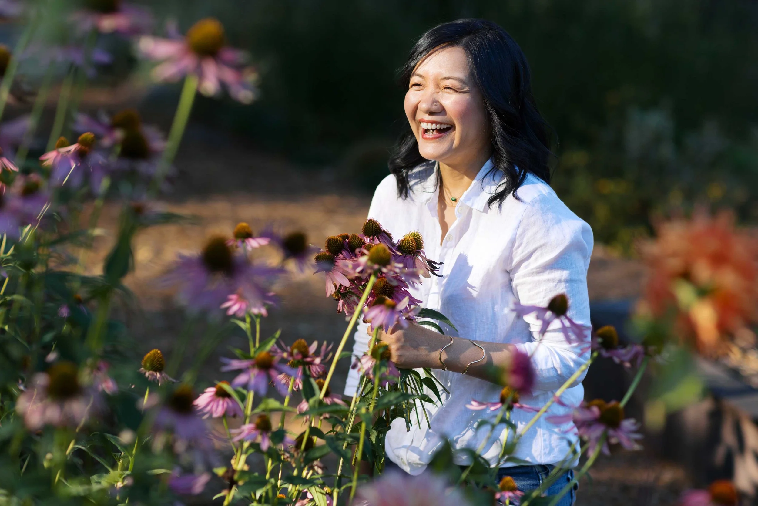 Woman with black hair and white shirt holding a bunch of Echinacea flowers and laughing