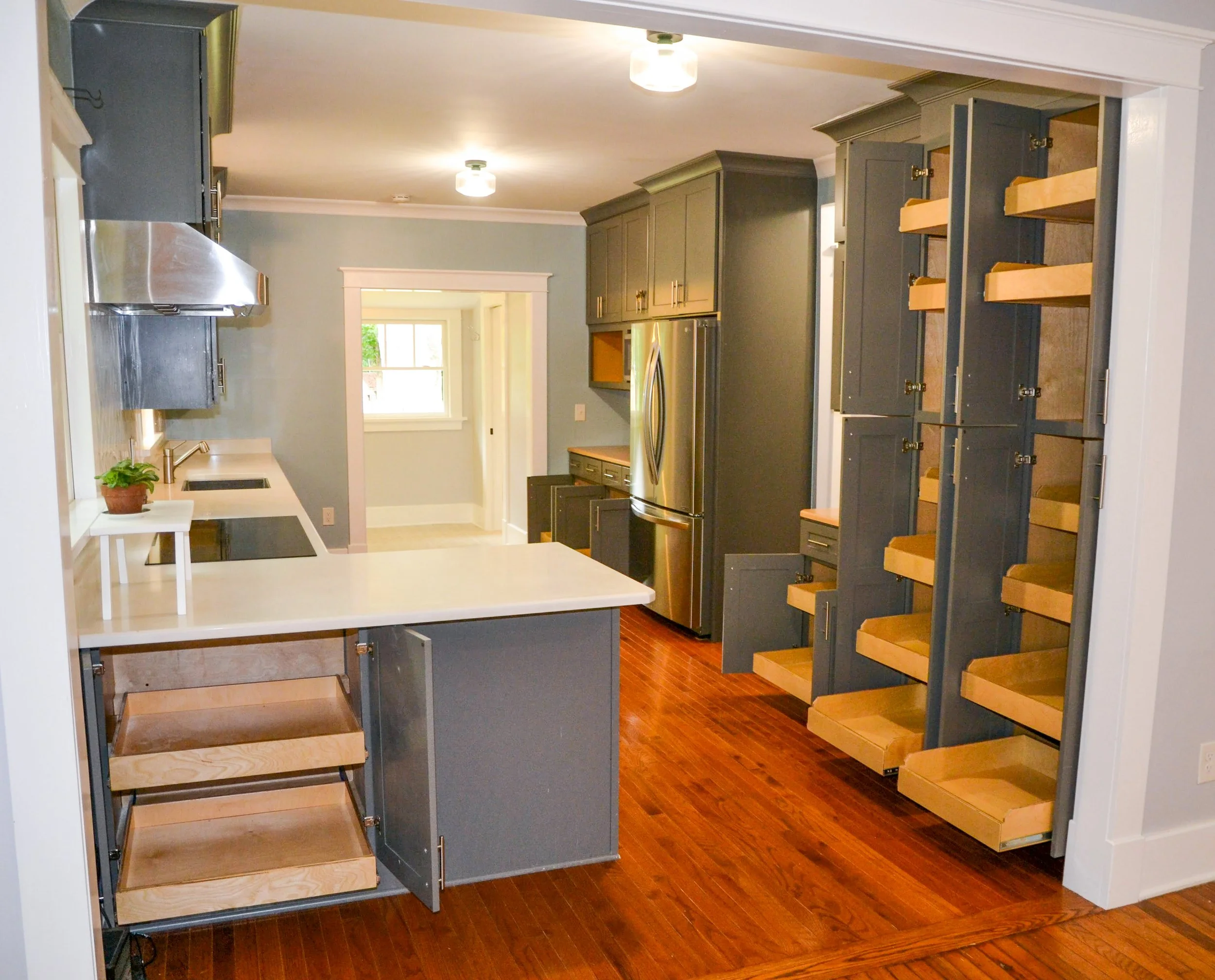 Custom modern renovated kitchen with dark gray cabinets, a stainless steel refrigerator, large cabinets with full-extension pull-out shelves and drawers, and a white countertop.