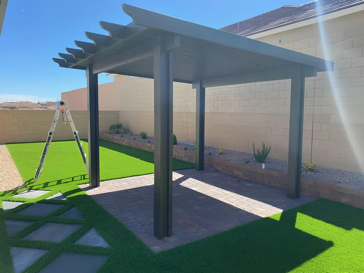 Backyard patio with a black metal pergola, artificial grass, a small garden bed with desert plants, and a ladder leaning against the pergola