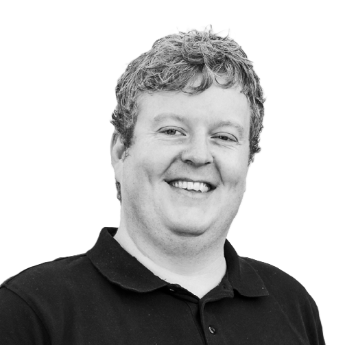 A smiling man with curly hair wearing a black polo shirt.