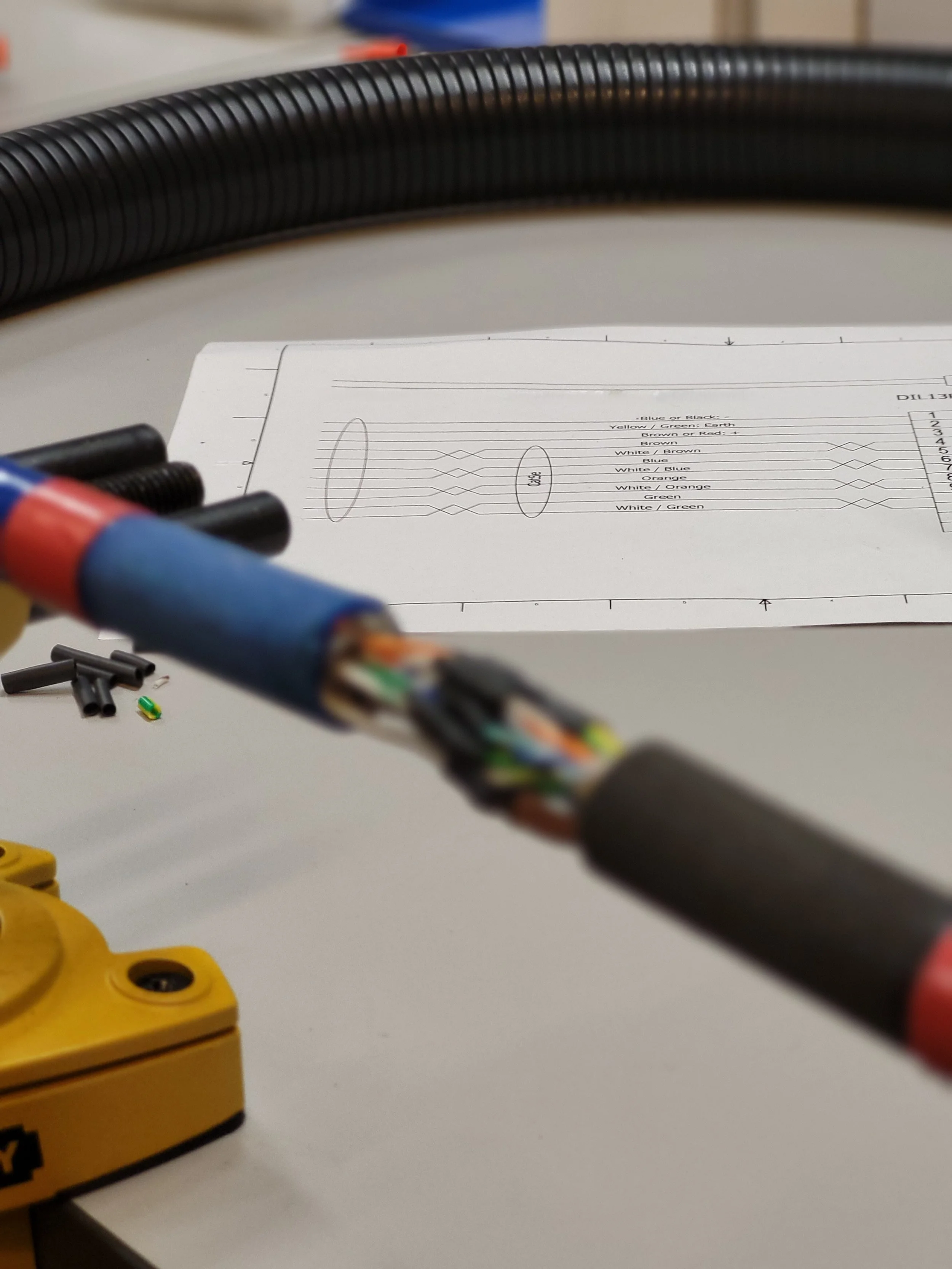 Close-up of an Ethernet cable with its outer sheath removed, exposing twisted pairs of wires inside, on a work surface with a schematic diagram in the background.