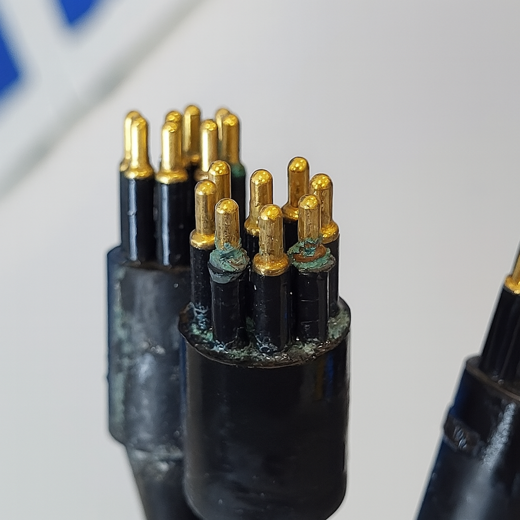 Close-up of a connector with multiple gold-tipped pins, some with green corrosion.