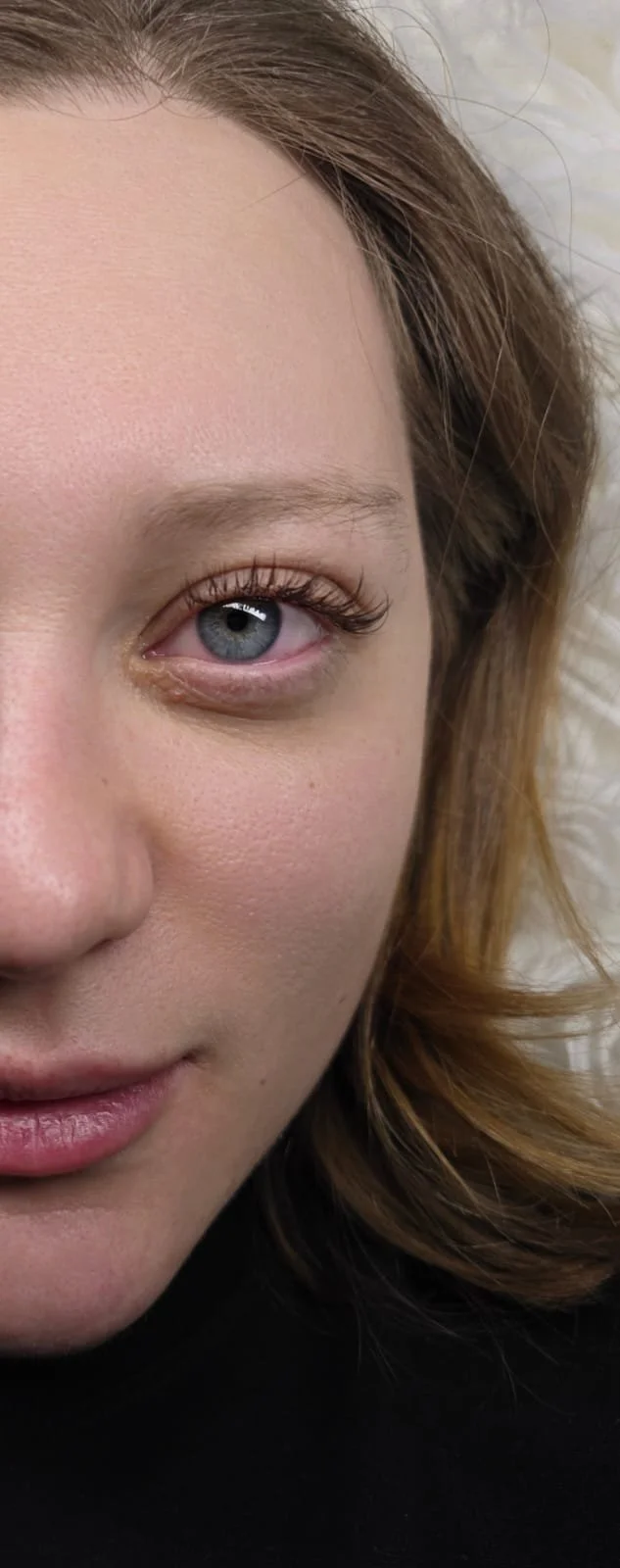 Close-up of a woman's face showing her blue eye, part of her brown hair, and her lips.