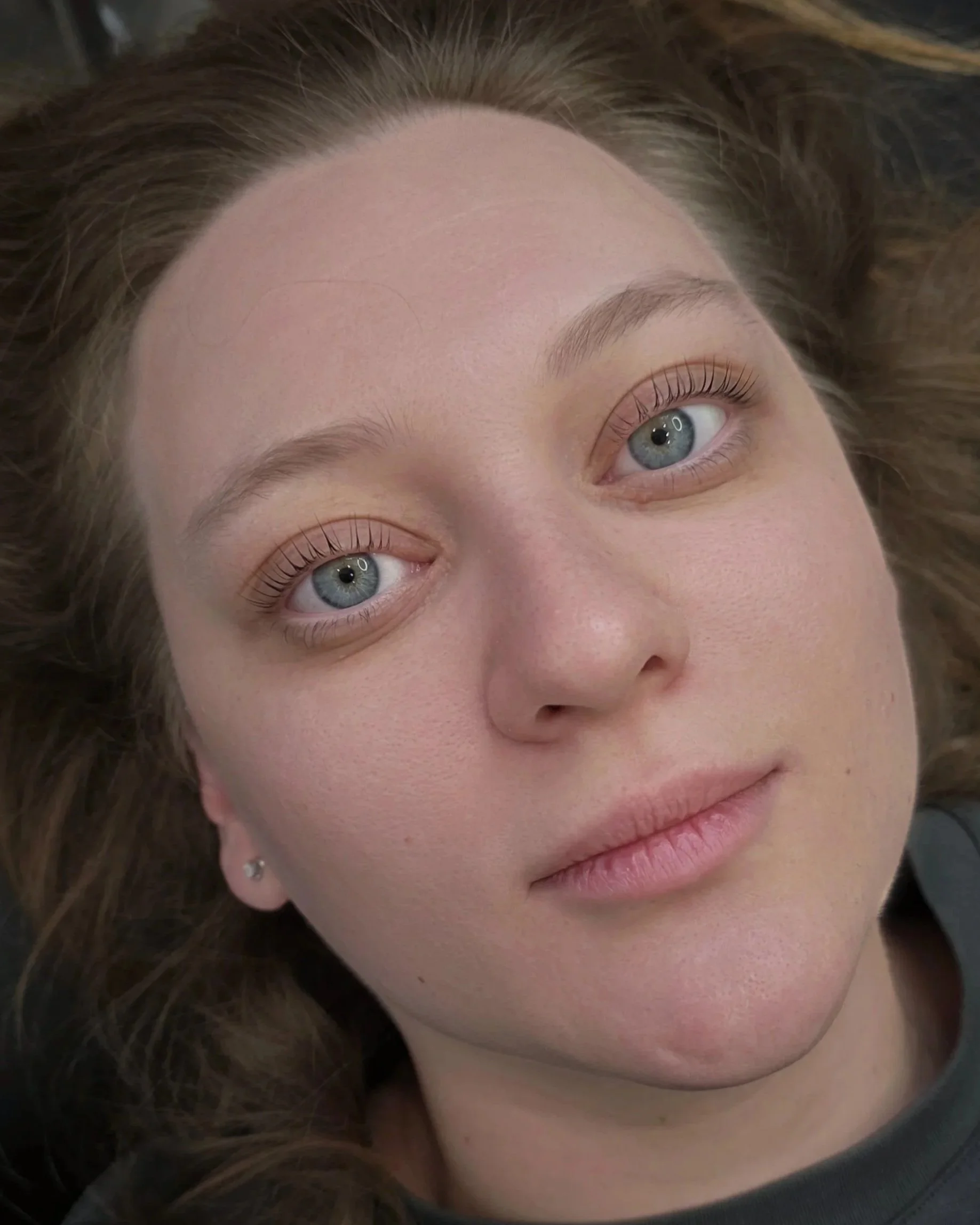 Close-up of a woman's face with blue eyes and curled eyelashes, lying down and looking at the camera.