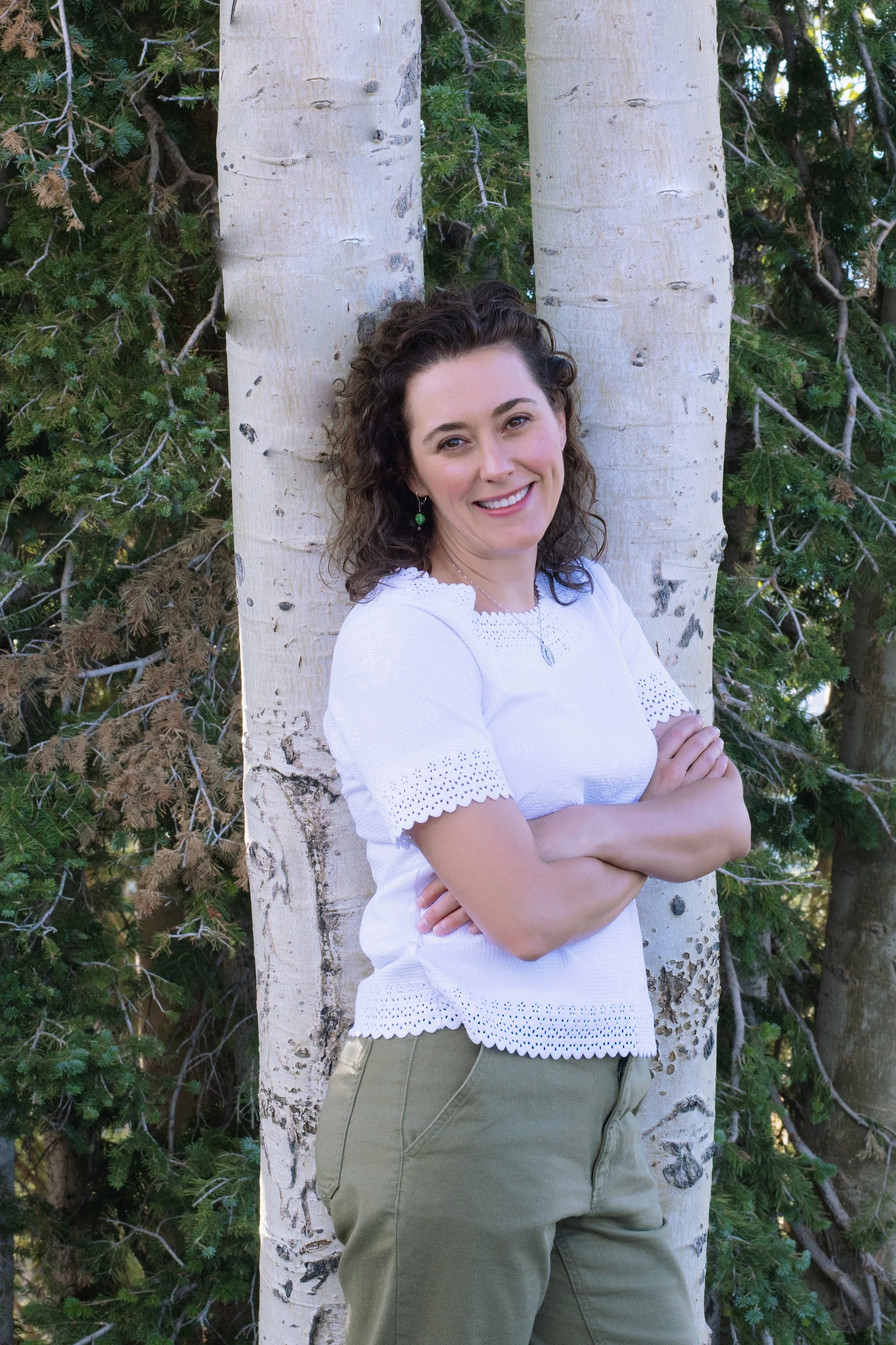 Curly haired women standing by an aspen tree smiling and happy