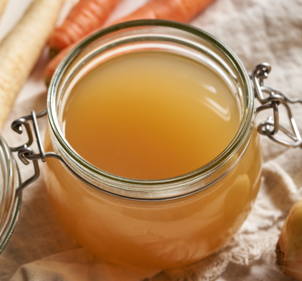 Rows of glass jars filled with bone broth on wooden shelves.