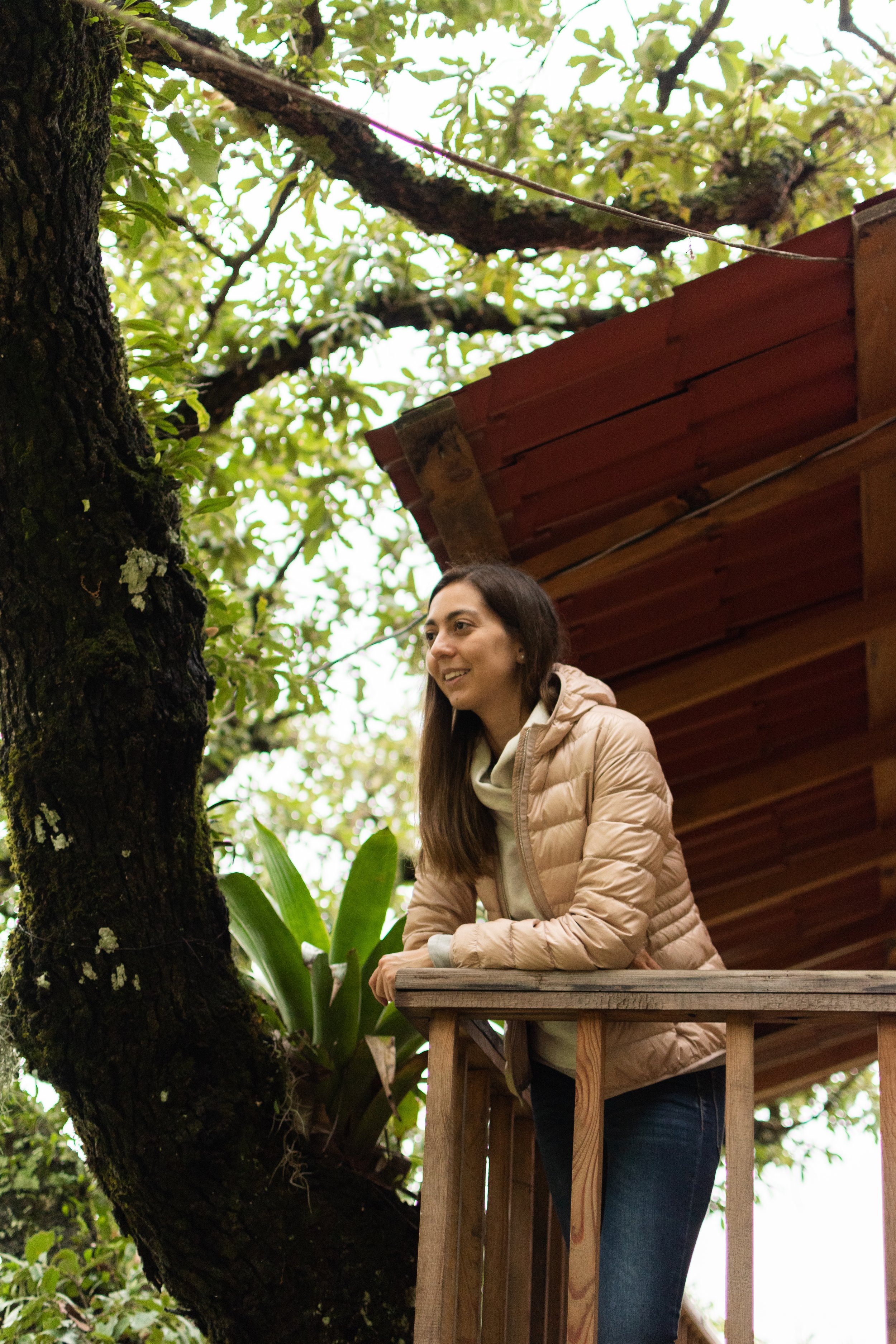 Mujer sonriendo en una estructura de madera en un entorno natural con árboles y plantas.