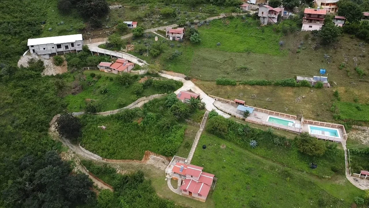 Vista aérea de una zona residencial en una colina, con varias casas, caminos pavimentados y una piscina enrejada.