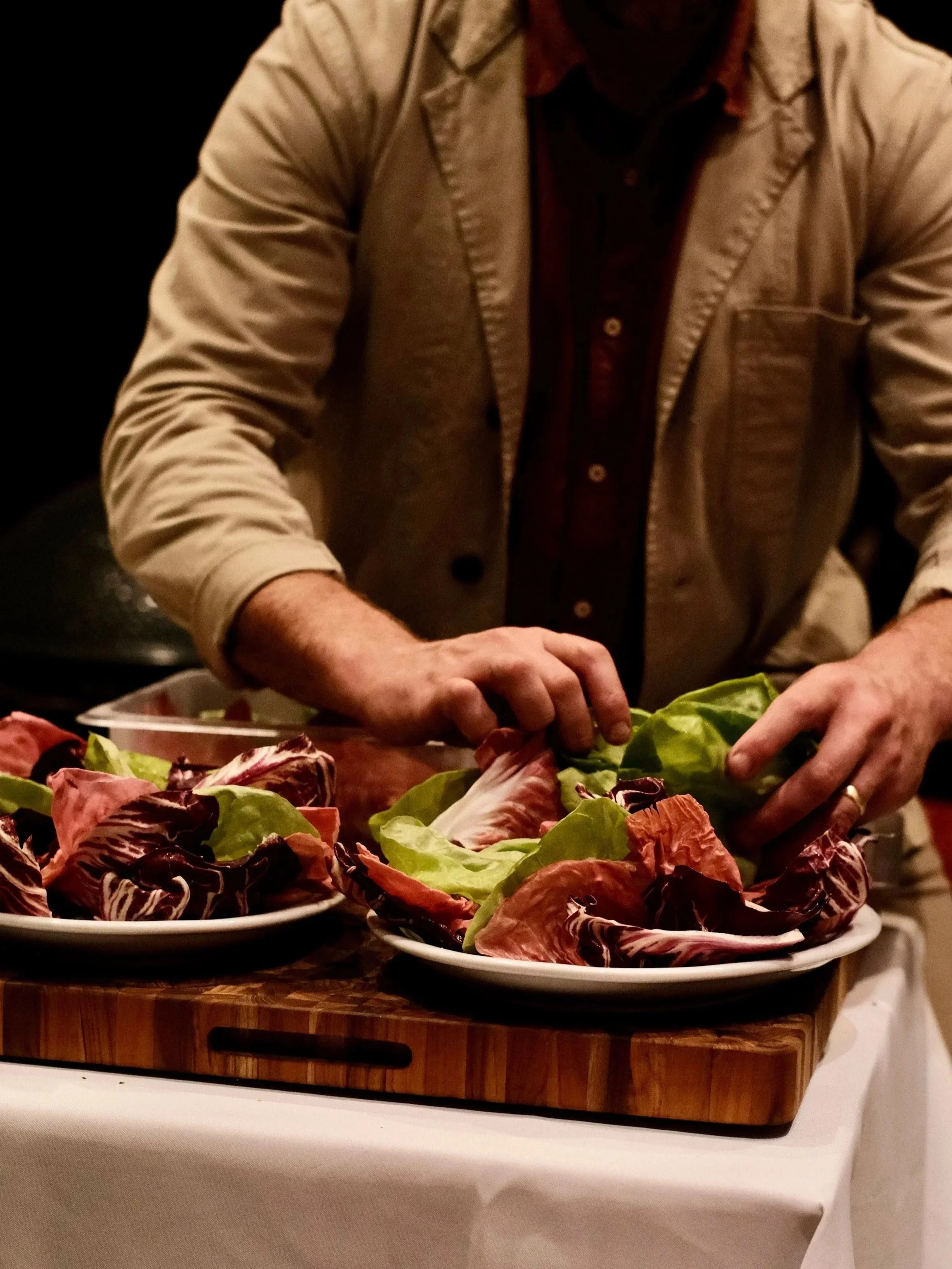 Person arranging various leafy greens and radicchio on plates for a meal.