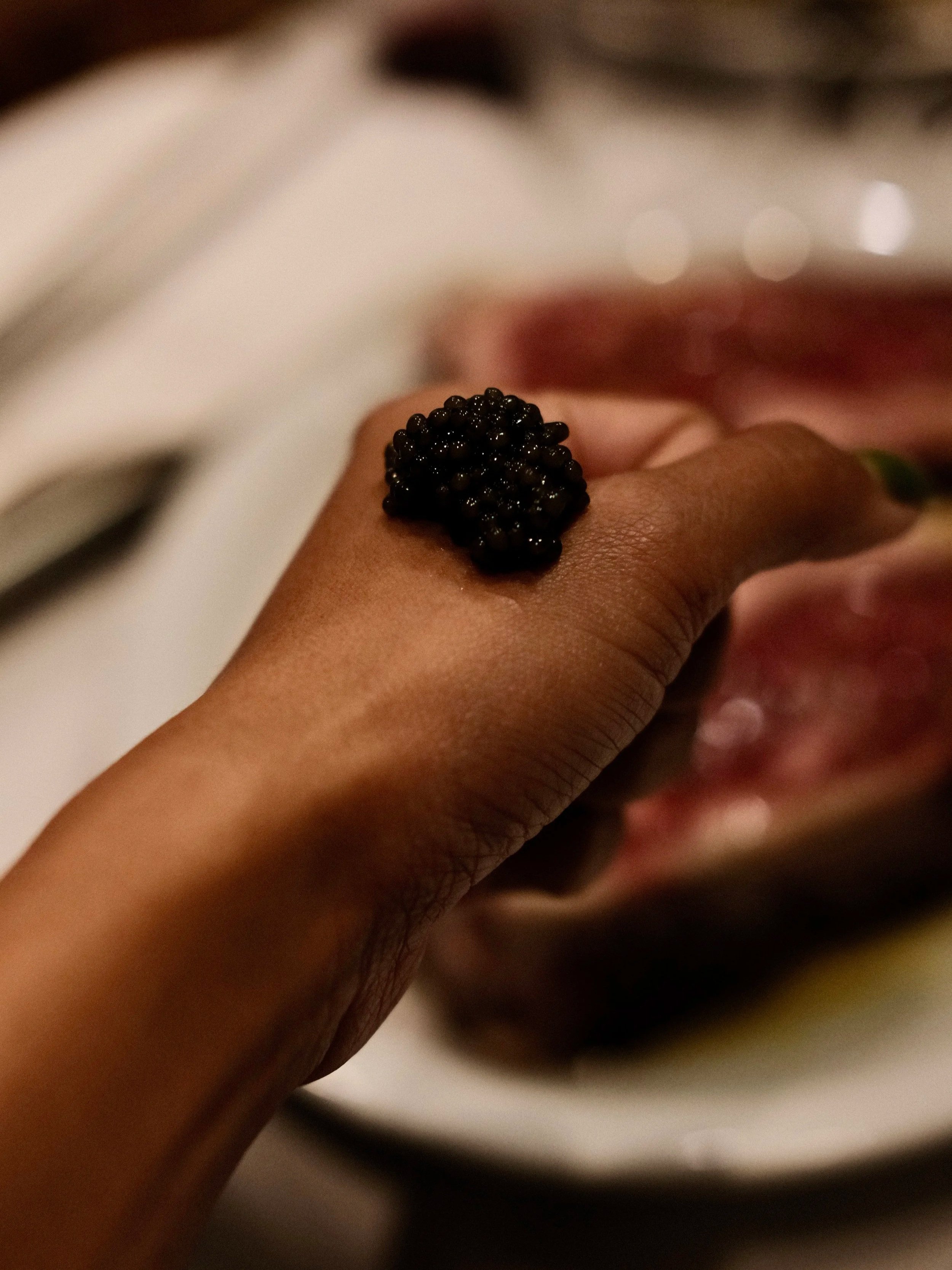 A hand with a black sturgeon caviar ring on the finger, placed over a blurred background.