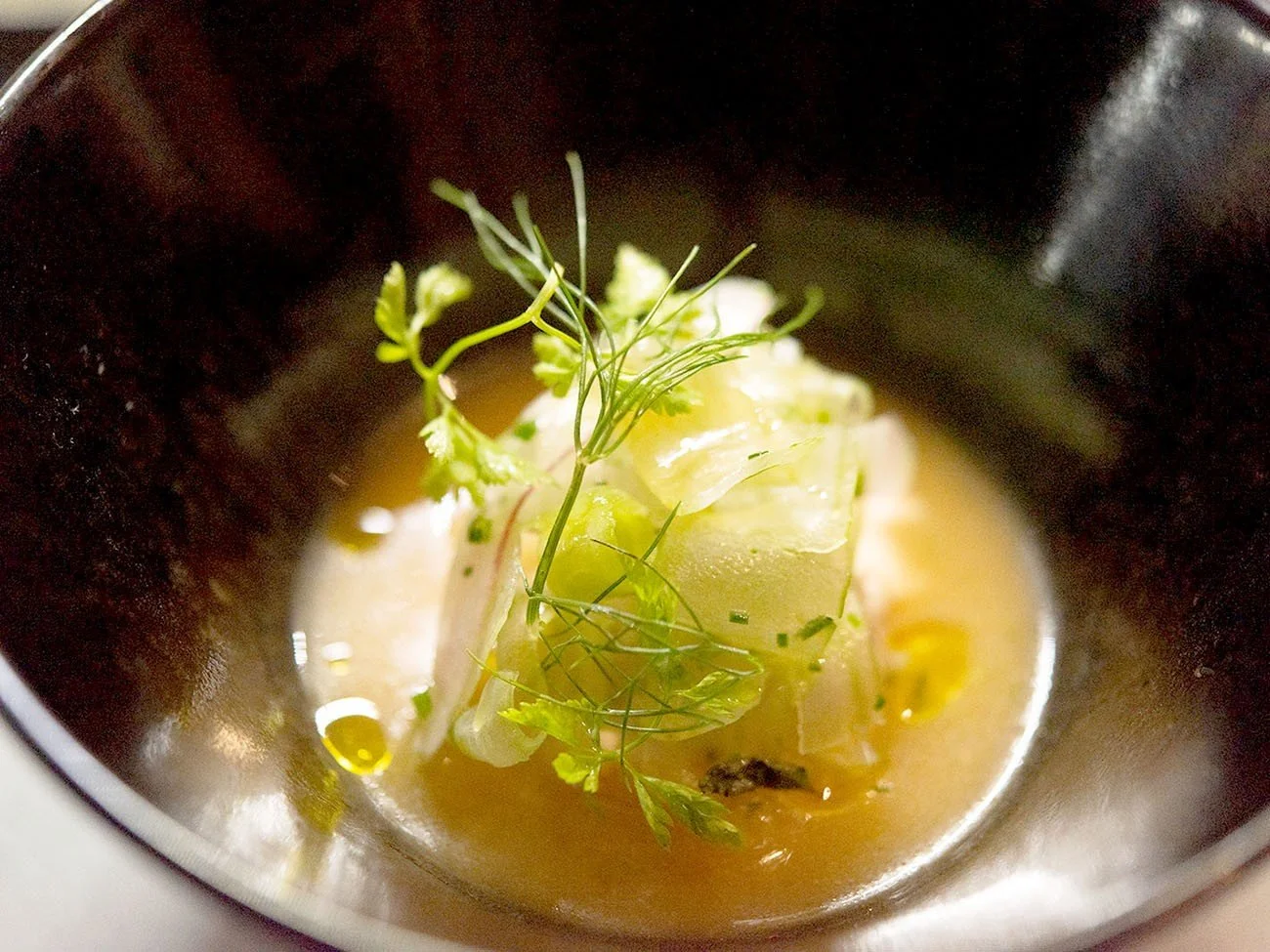 Soup with a cube of fish or tofu, garnished with fresh herbs and a drizzle of oil