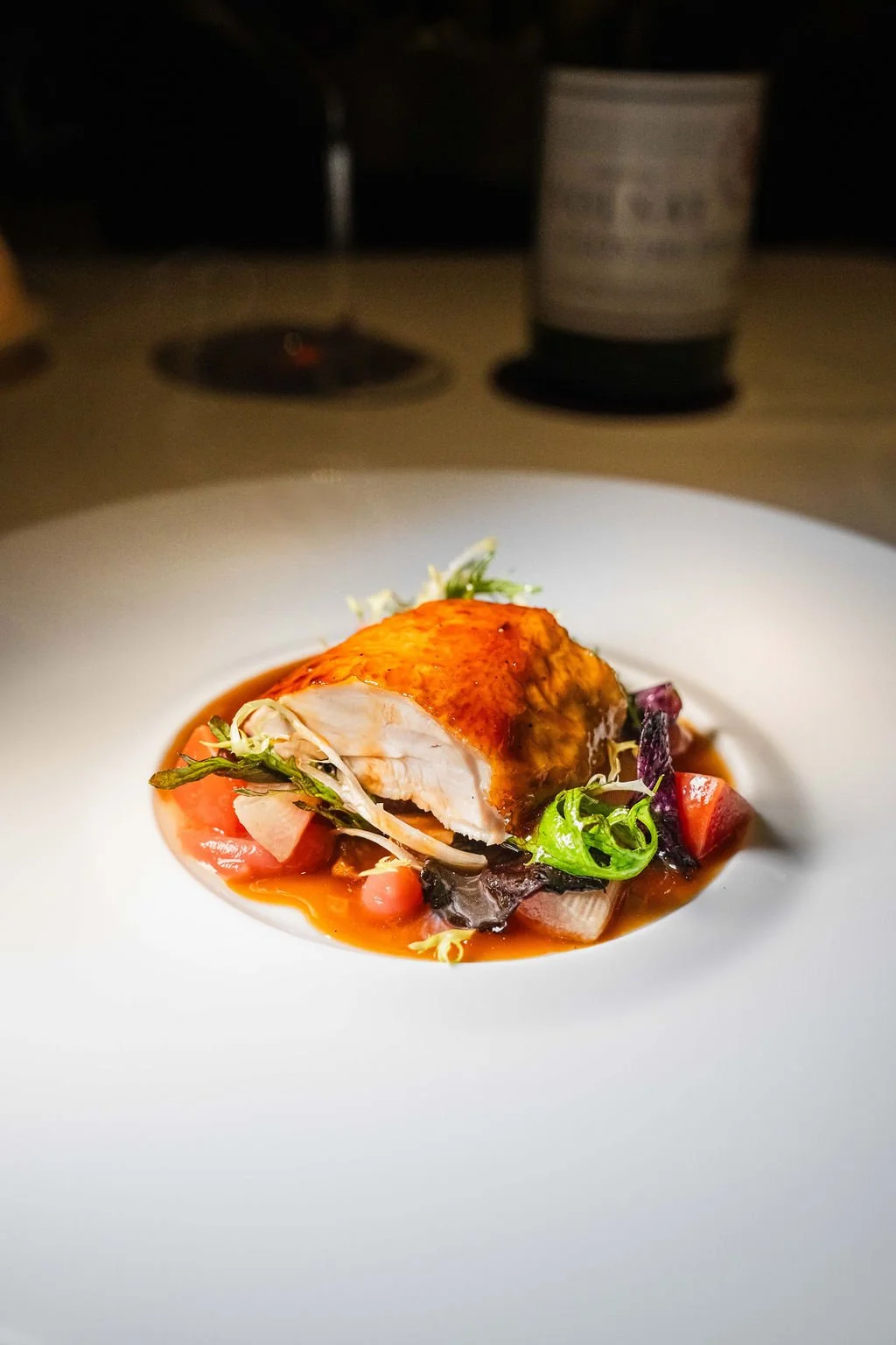 A plated dish featuring a piece of cooked chicken with crispy skin, served on a bed of mixed vegetables and sauce.
