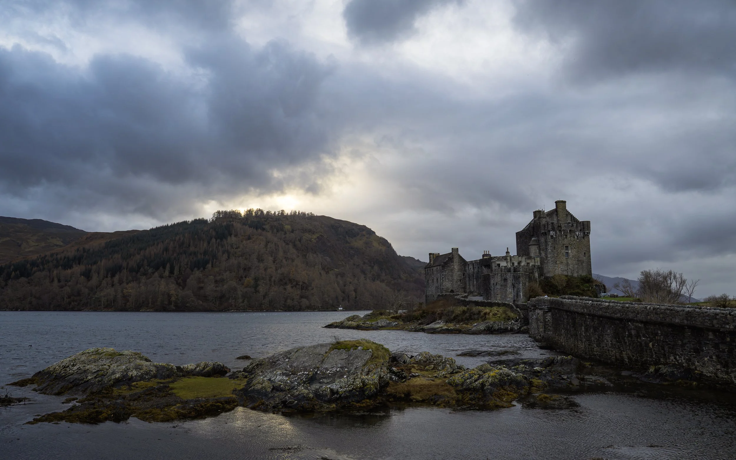 A castle by the water under cloudy skies with mountains in the background. Scotland.