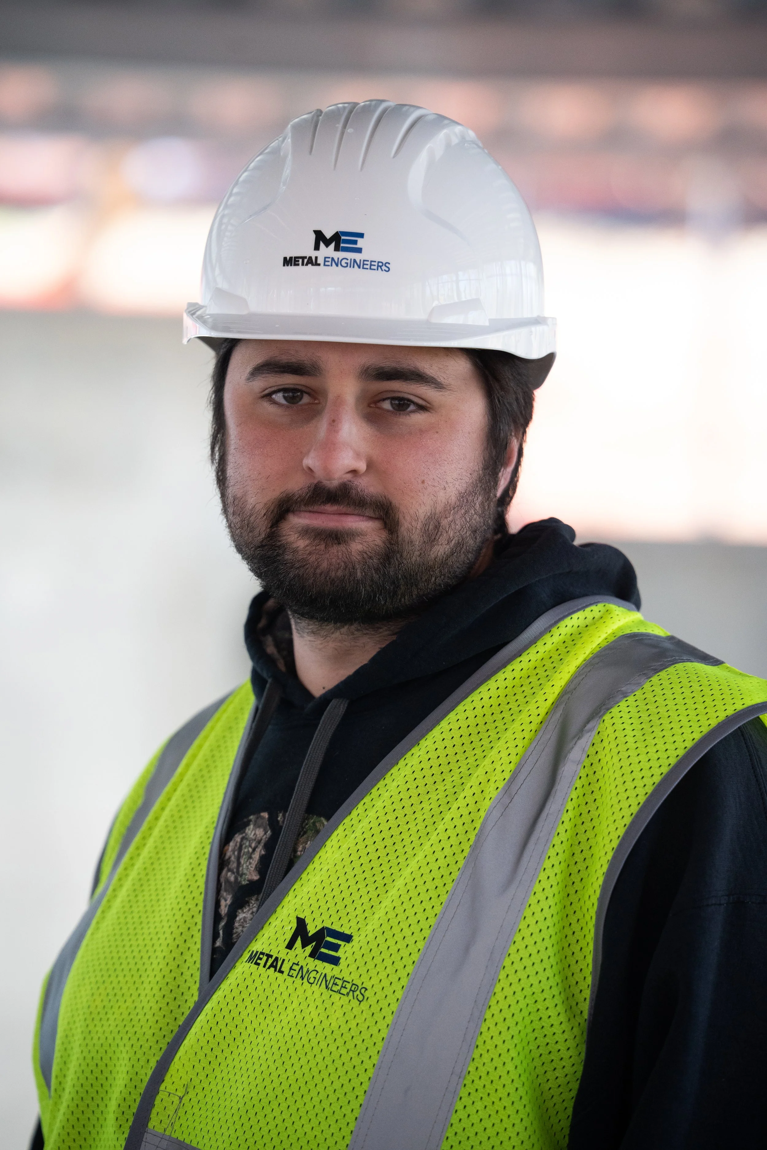A man wearing a white safety helmet and a yellow reflective vest featuring the logo of Metal Engineers.
