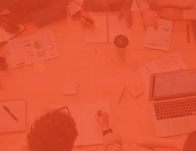 People working around a table with laptops, notebooks, and pens.