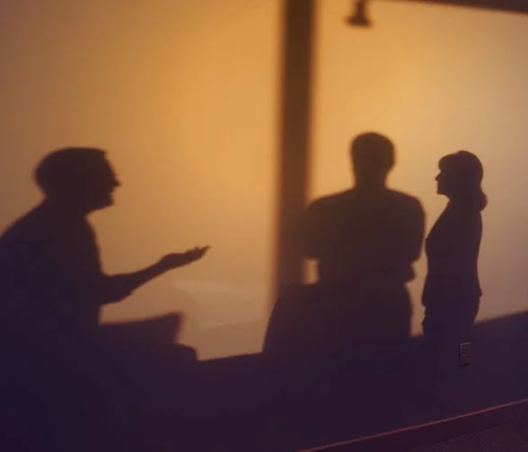 Silhouettes of three people having a conversation indoors, with a warm, softly lit background.