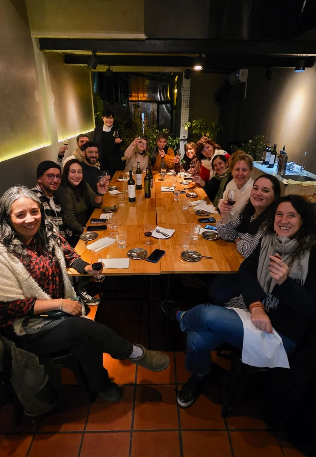 Grupo de personas celebrando en un restaurante, sentados alrededor de una mesa de madera con copas de vino.