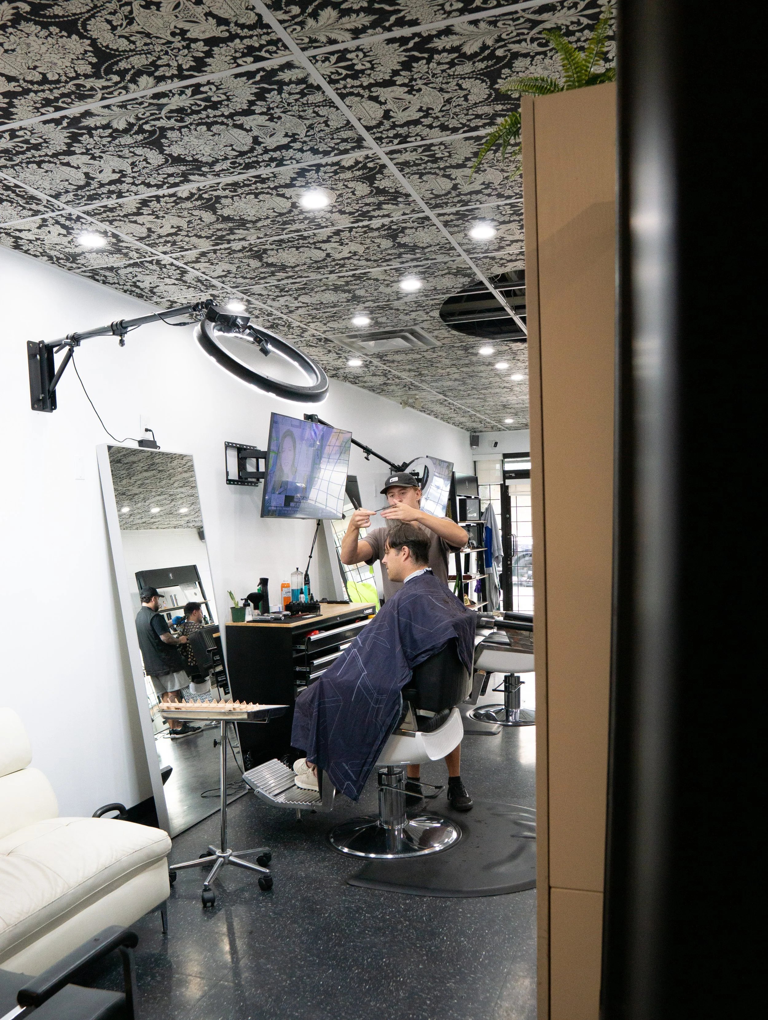 A barber giving a haircut to a customer in a modern barber shop with LED ceiling lights, a large mirror, and hairdressing tools.