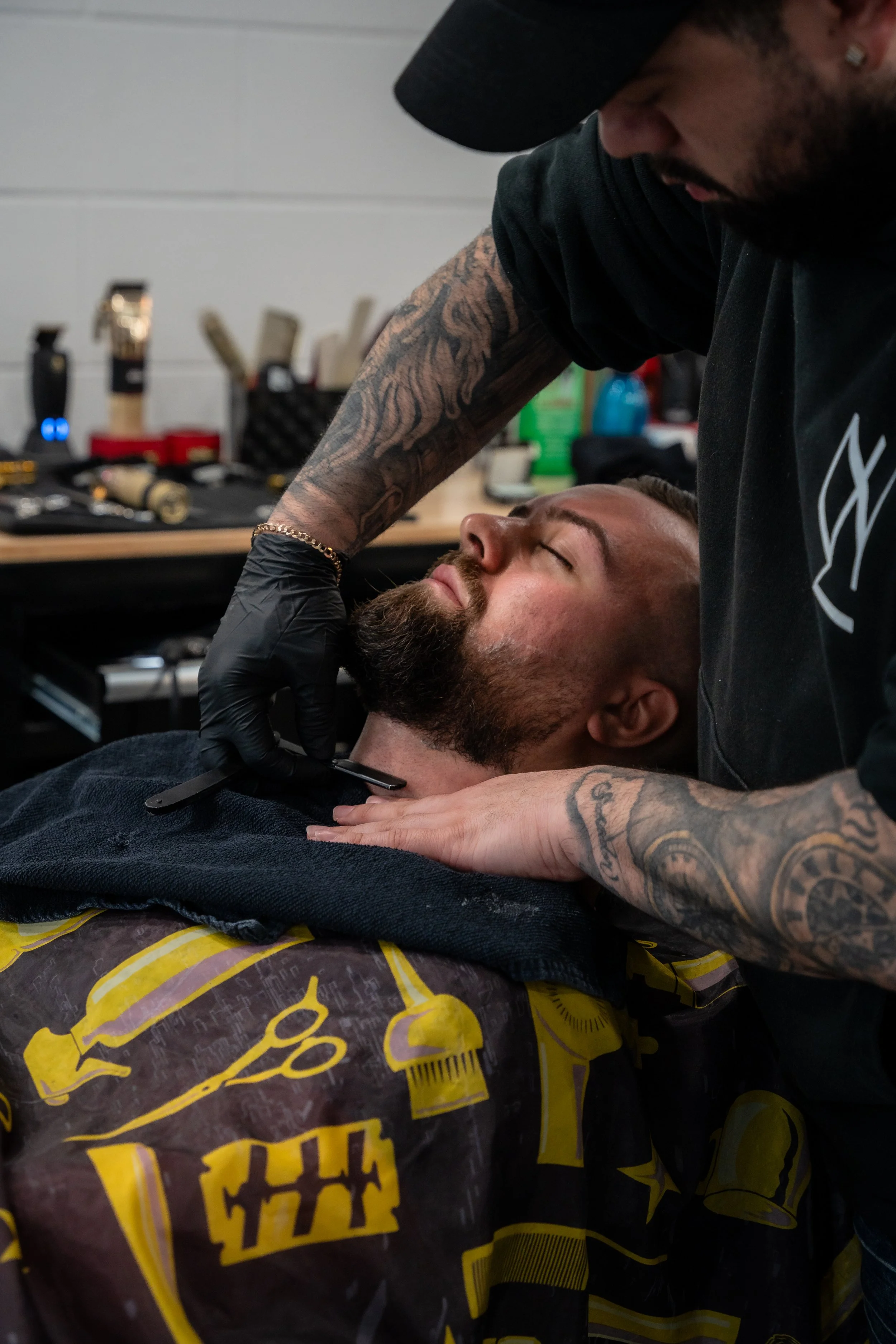A barber shaving a man's beard with a straight razor in a barbershop.