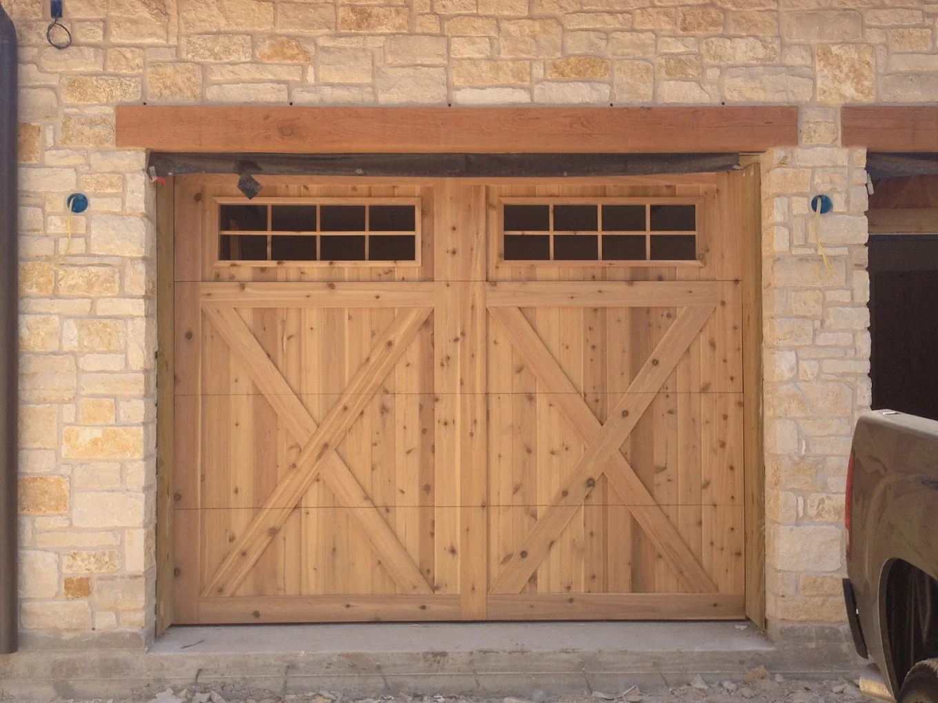 A wooden garage door with windows at the top, set in a brick wall with a wooden beam above.