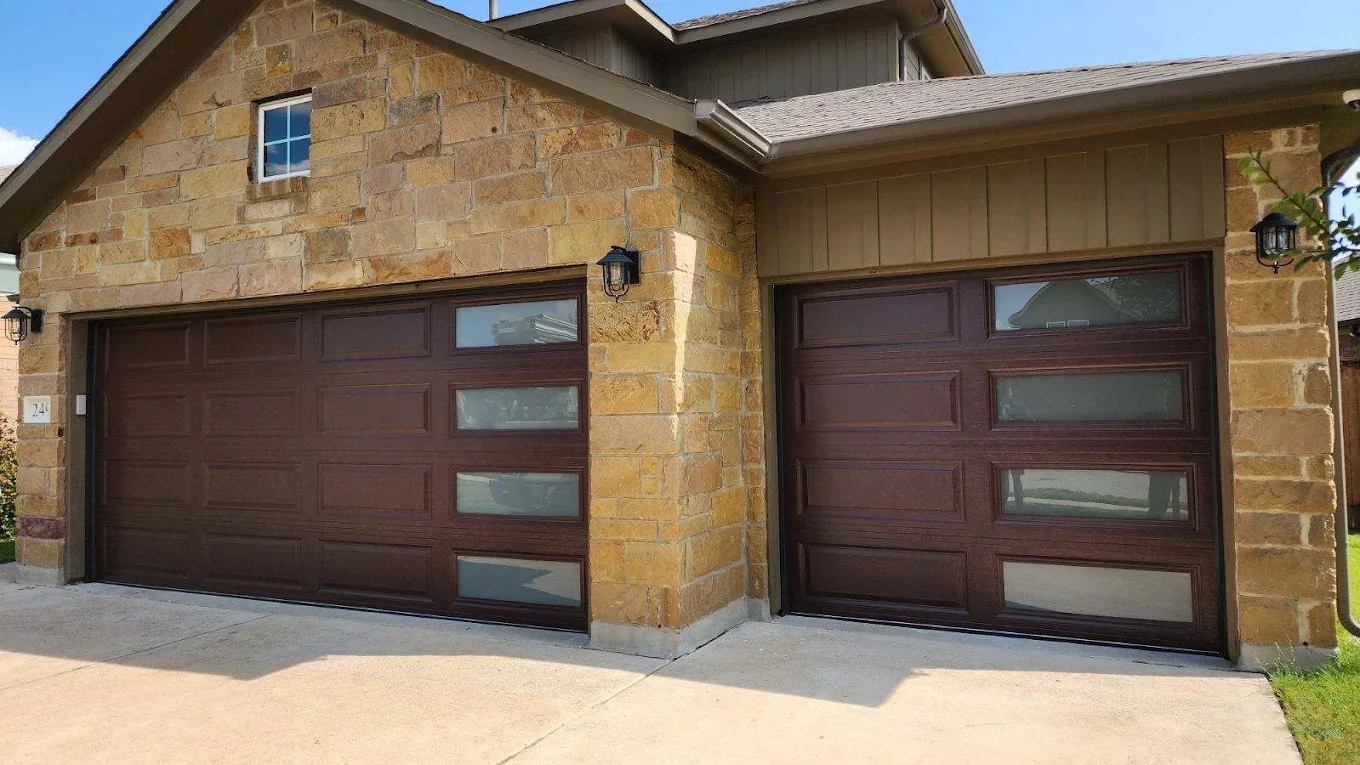 Two garage doors with dark brown panels and frosted glass windows, on either side of a stone and wooden house.