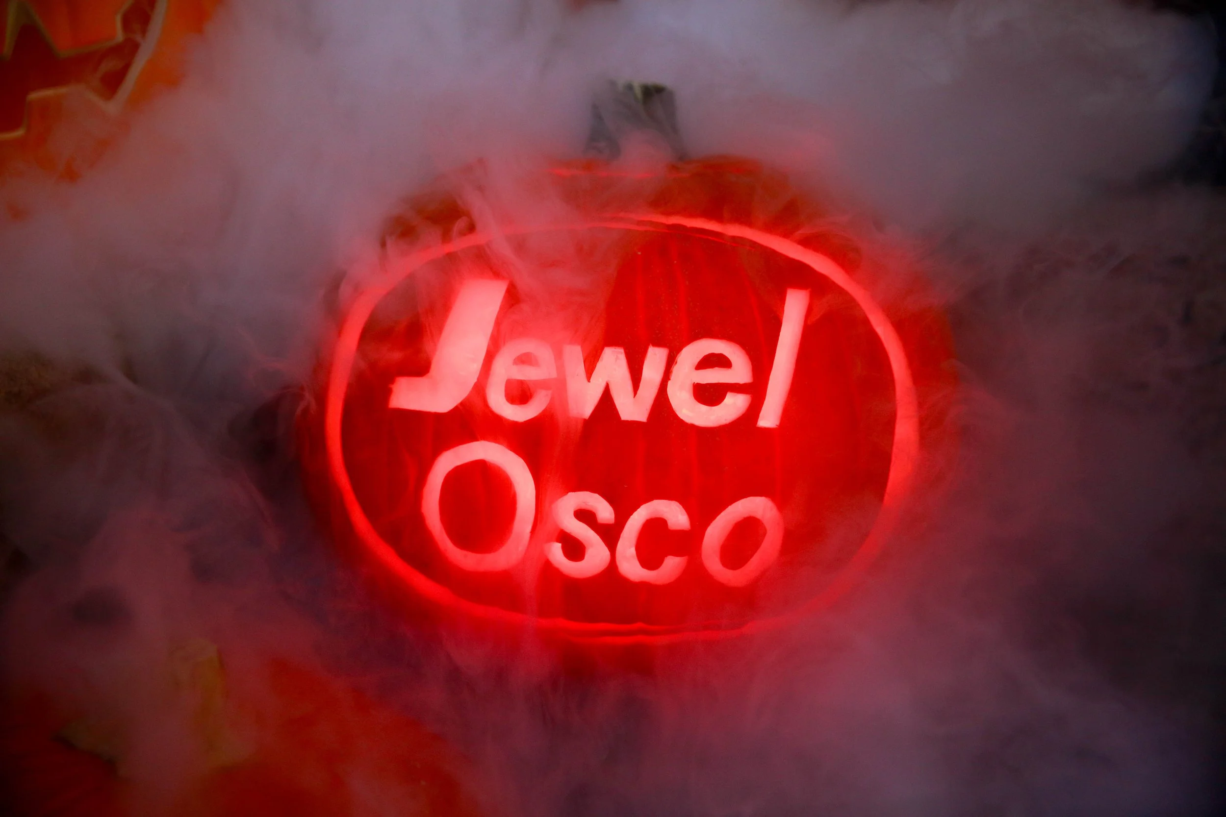 Carved pumpkin displaying the words 'Jewel Osco' surrounded by fog or smoke.