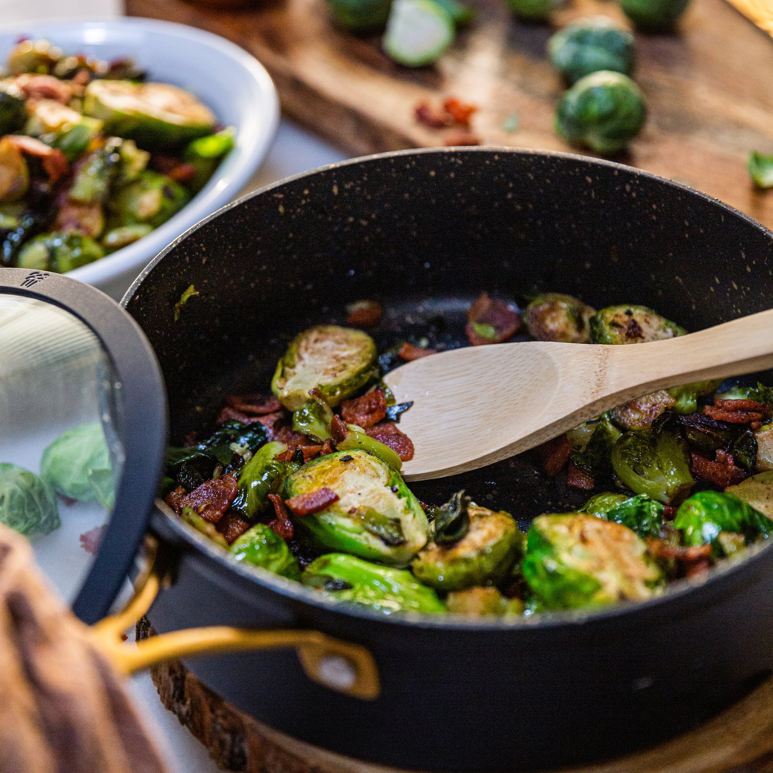 Cooked Brussels sprouts and bacon in a black frying pan on a wooden surface