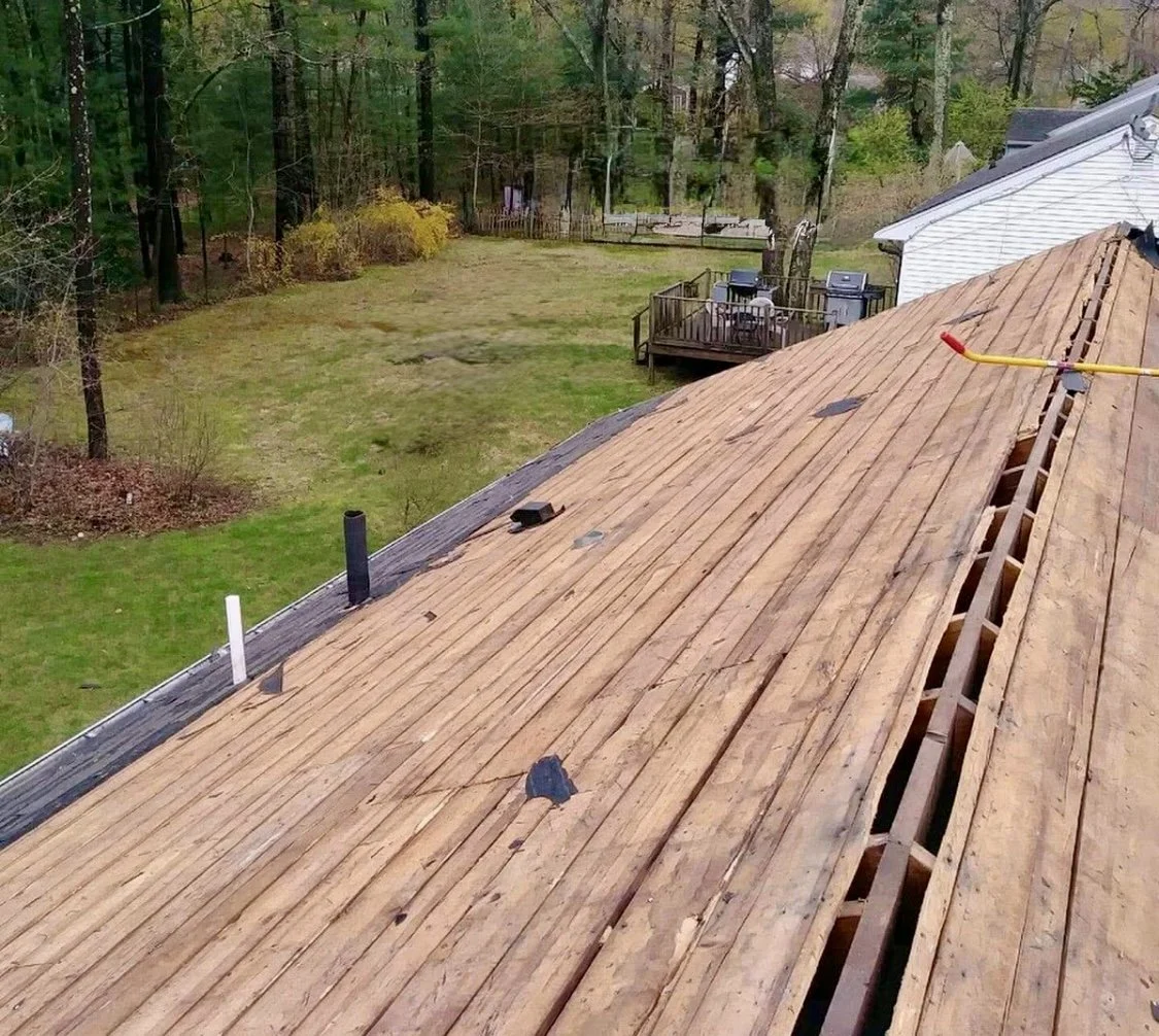 A house roof undergoing repairs by Signature Reno Group with some wooden shingles removed, revealing the wooden structure underneath.