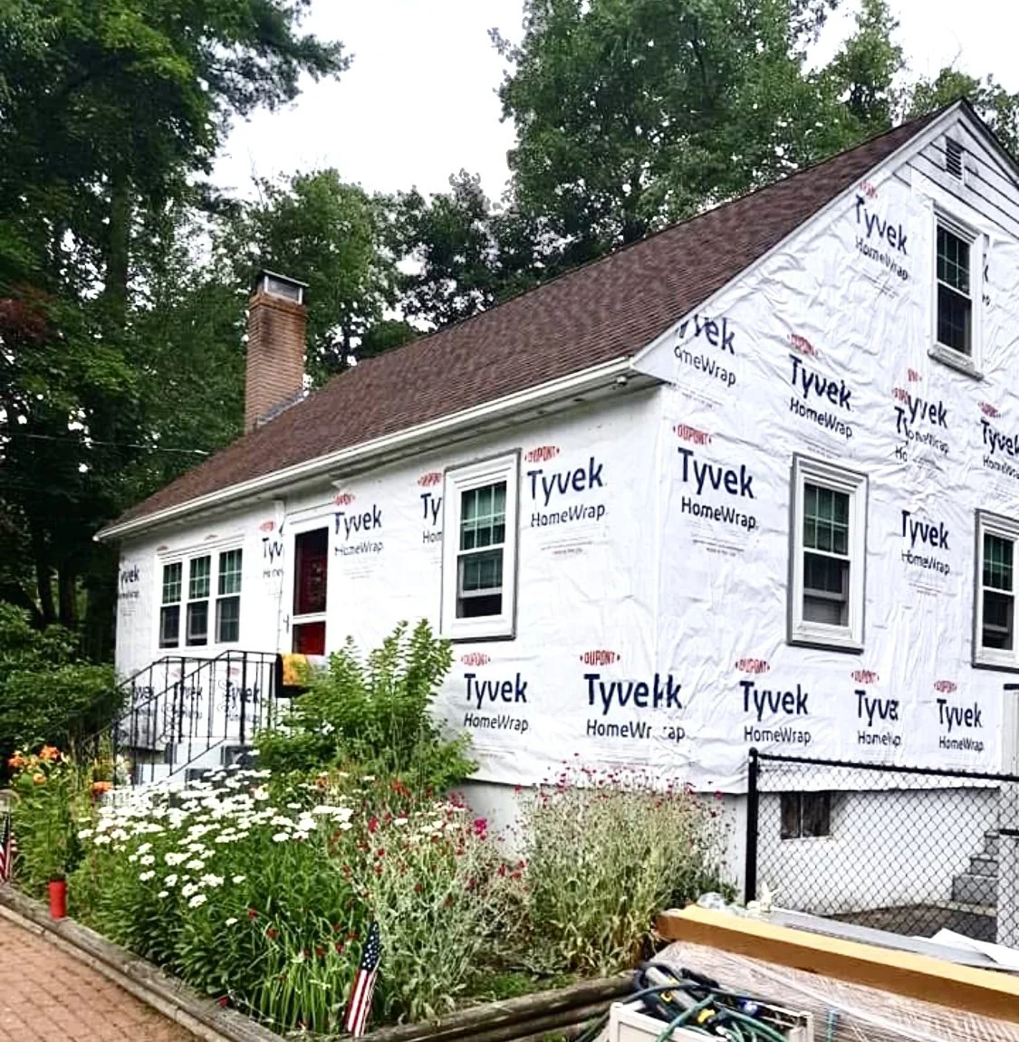 A house undergoing exterior renovation with Tyvek HomeWrap on the walls. This Signature Reno Group project features vinyl siding replacement for a Cape.