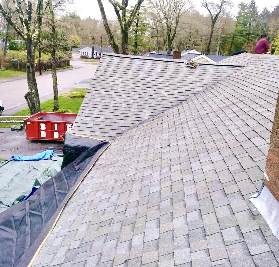 View of a house roof with shingles under repair by Signature Reno Group, showing one of our workers on the roof.