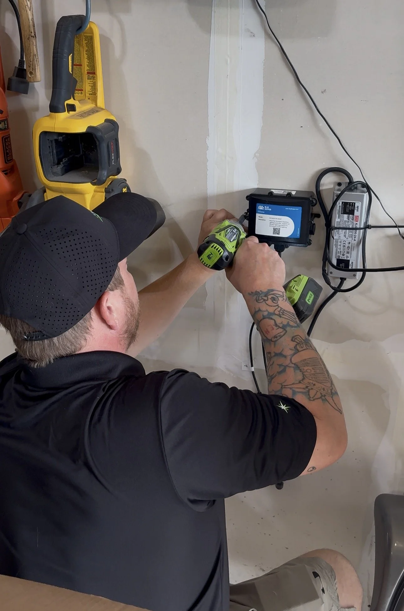 man facing a wall, with a drill in his hand, attaching a power pack for permanent lights in a garage