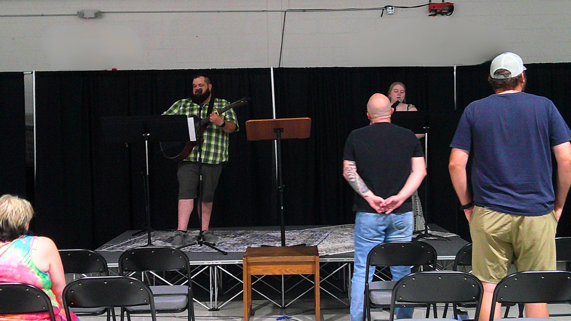 Musicians performing on stage at an indoor event, with audience members watching.