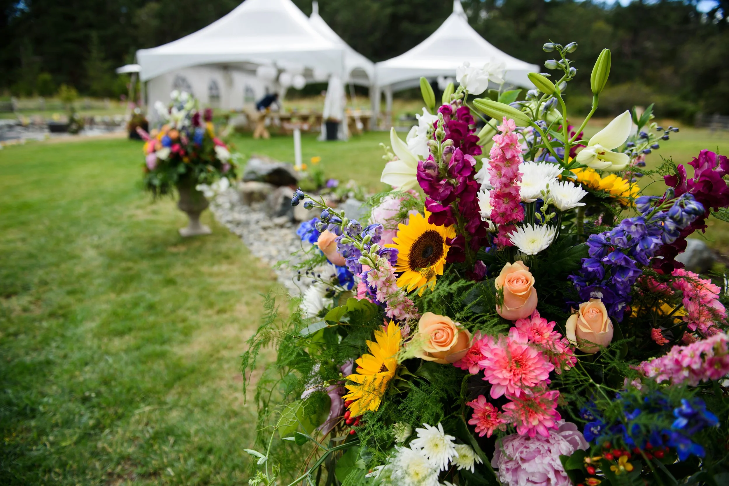 Colourful floral display on grass in large garden with marquee in background
