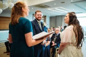 Kimberley Jones speaking to a couple during a wedding ceremony in a modern indoor venue.