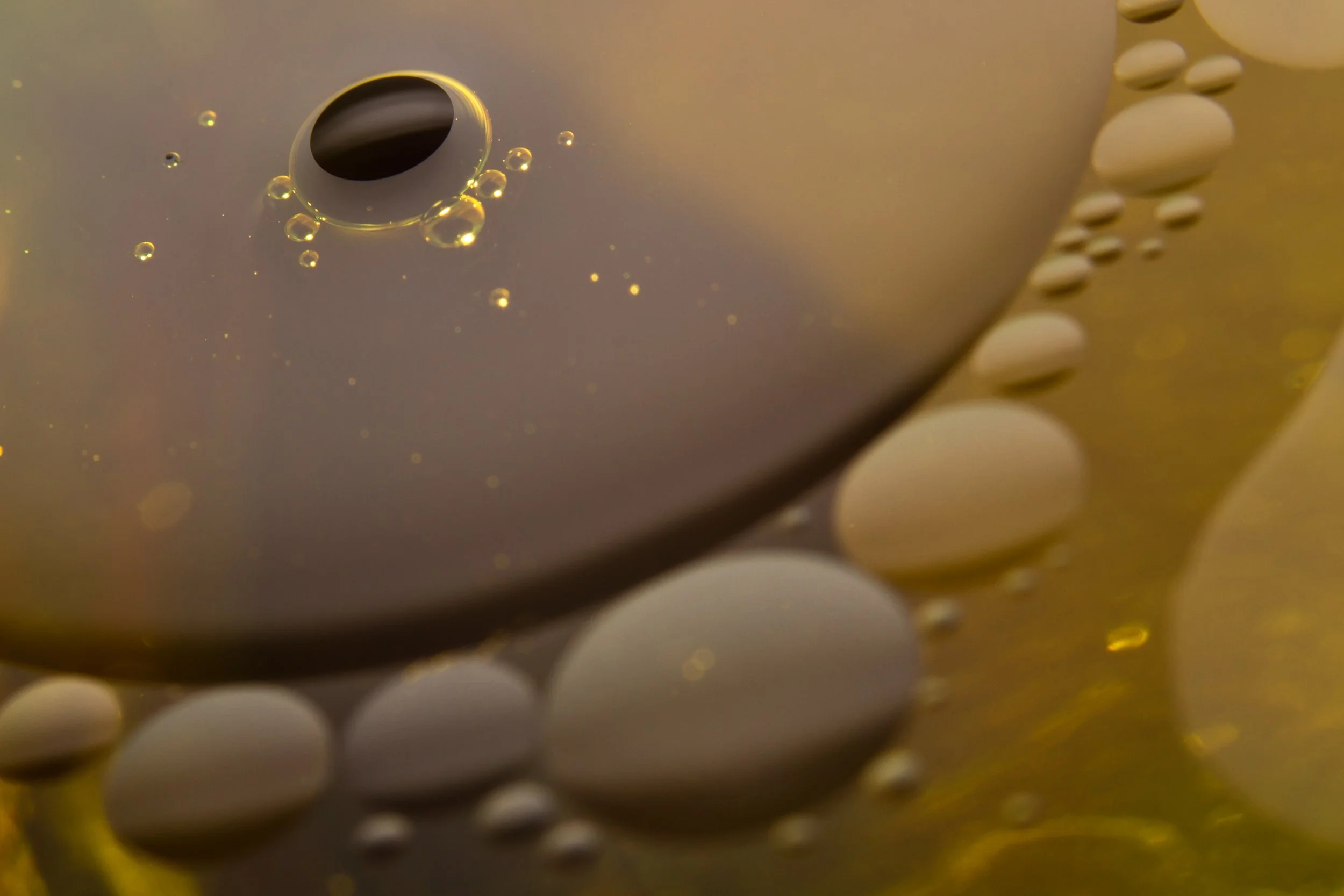Gotas de aceite en una superficie, con una burbuja de aire en el centro, mostrando diferentes tamaños y reflejos.