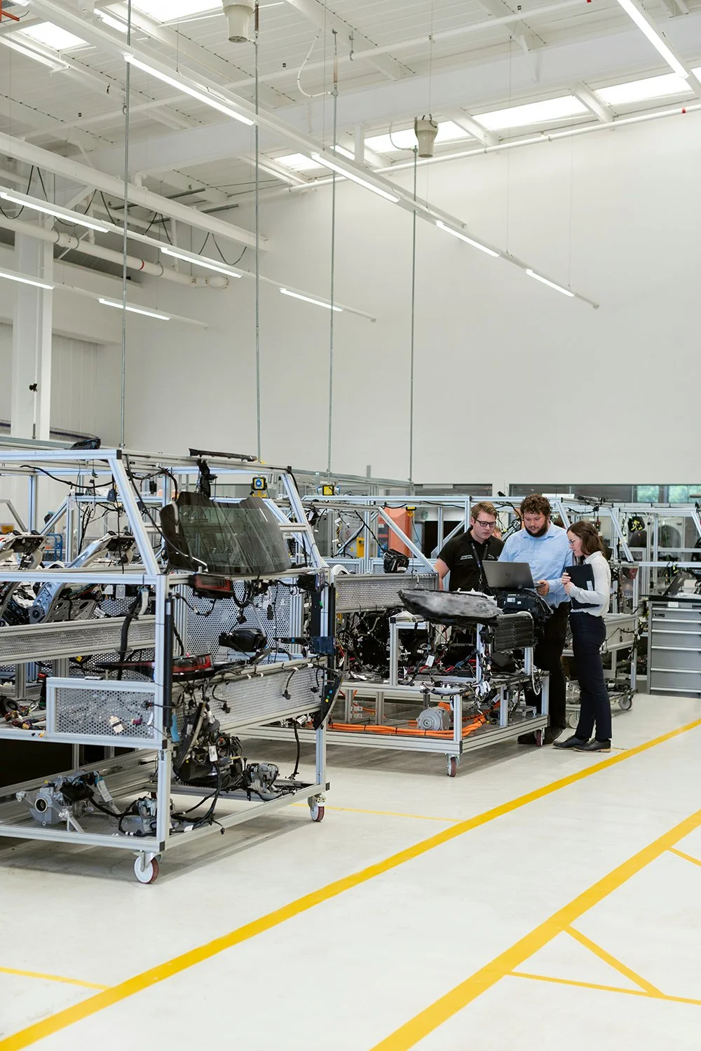 Tres personas trabajando en una línea de ensamblaje de componentes electrónicos en un entorno industrial bien iluminado.