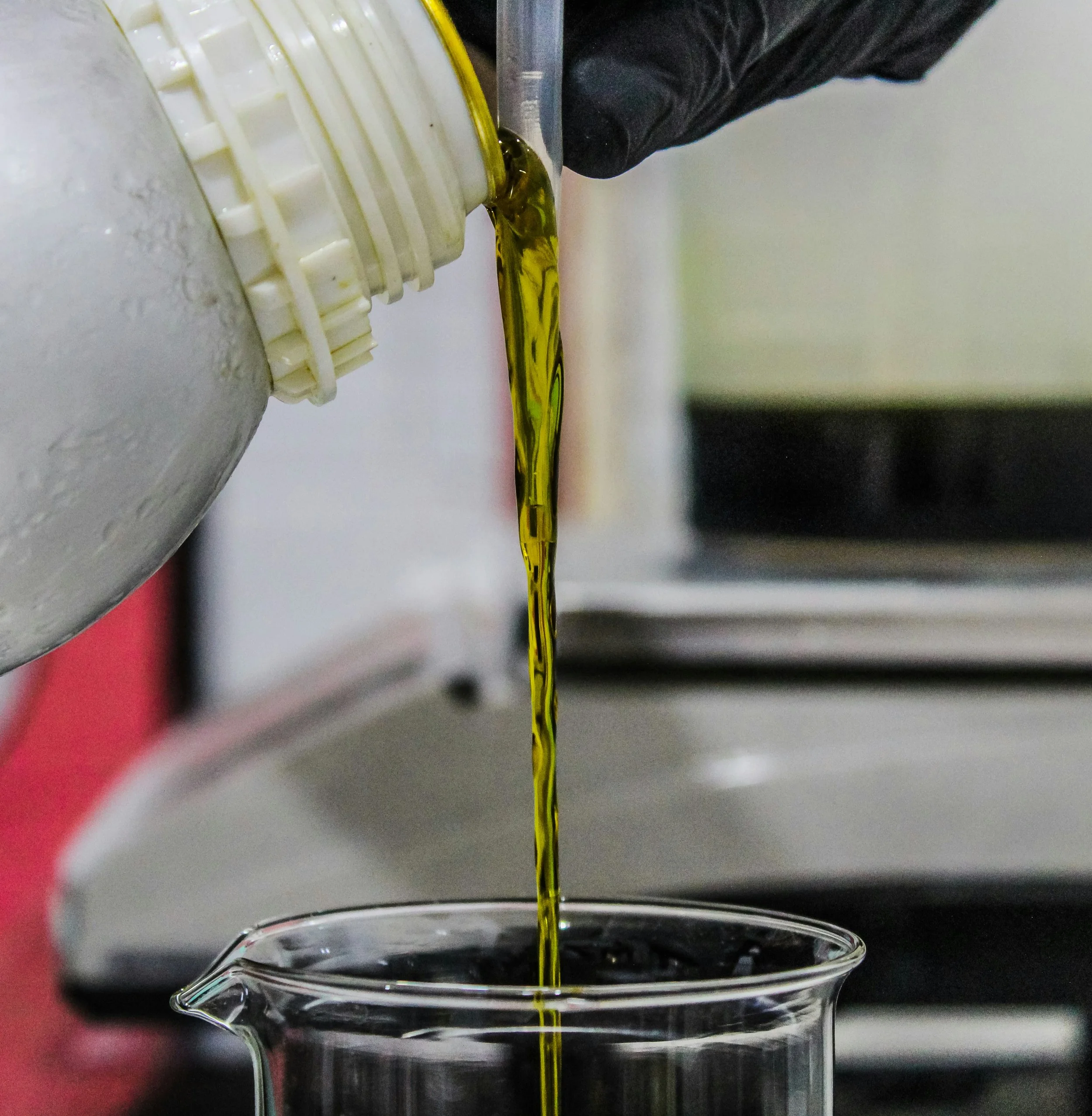 Aceite saliendo de un envase y siendo vertido en un vaso de laboratorio.