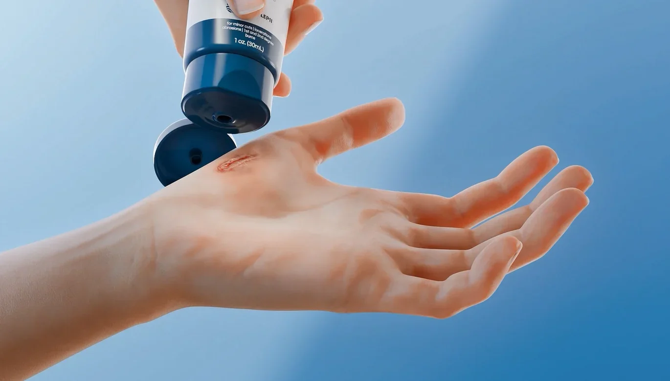 A hand with a cut on the thumb is receiving ointment from a tube against a blue background.