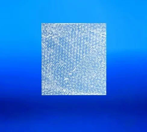 Close-up of a textured, transparent glass or plastic sheet with a patterned surface, placed against a blue gradient background.