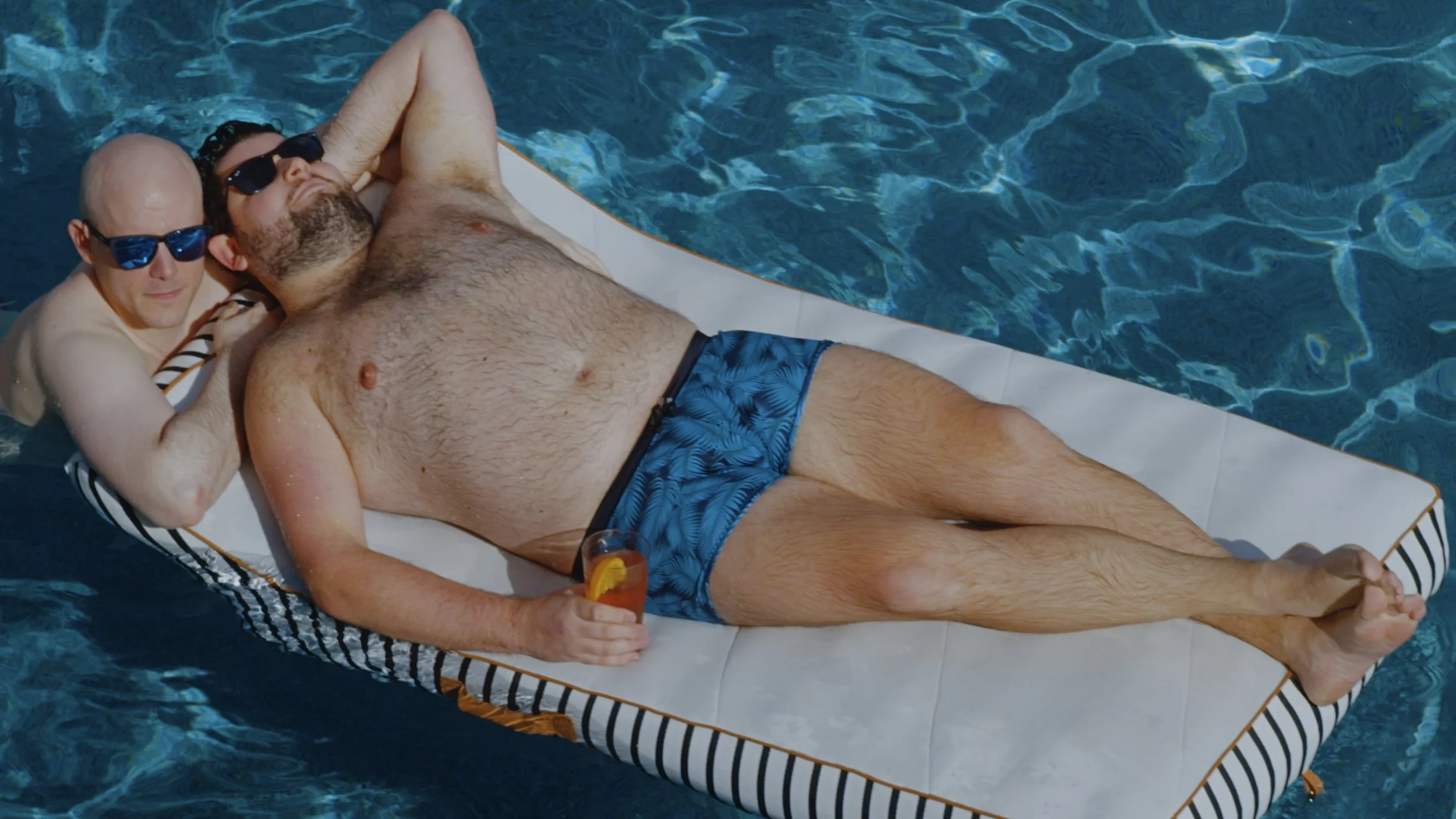 Actors Nicholas Molencupp and Aaron Goldenberg relaxing in a swimming pool as Nick and Wes in a scene from the queer indie film In Between