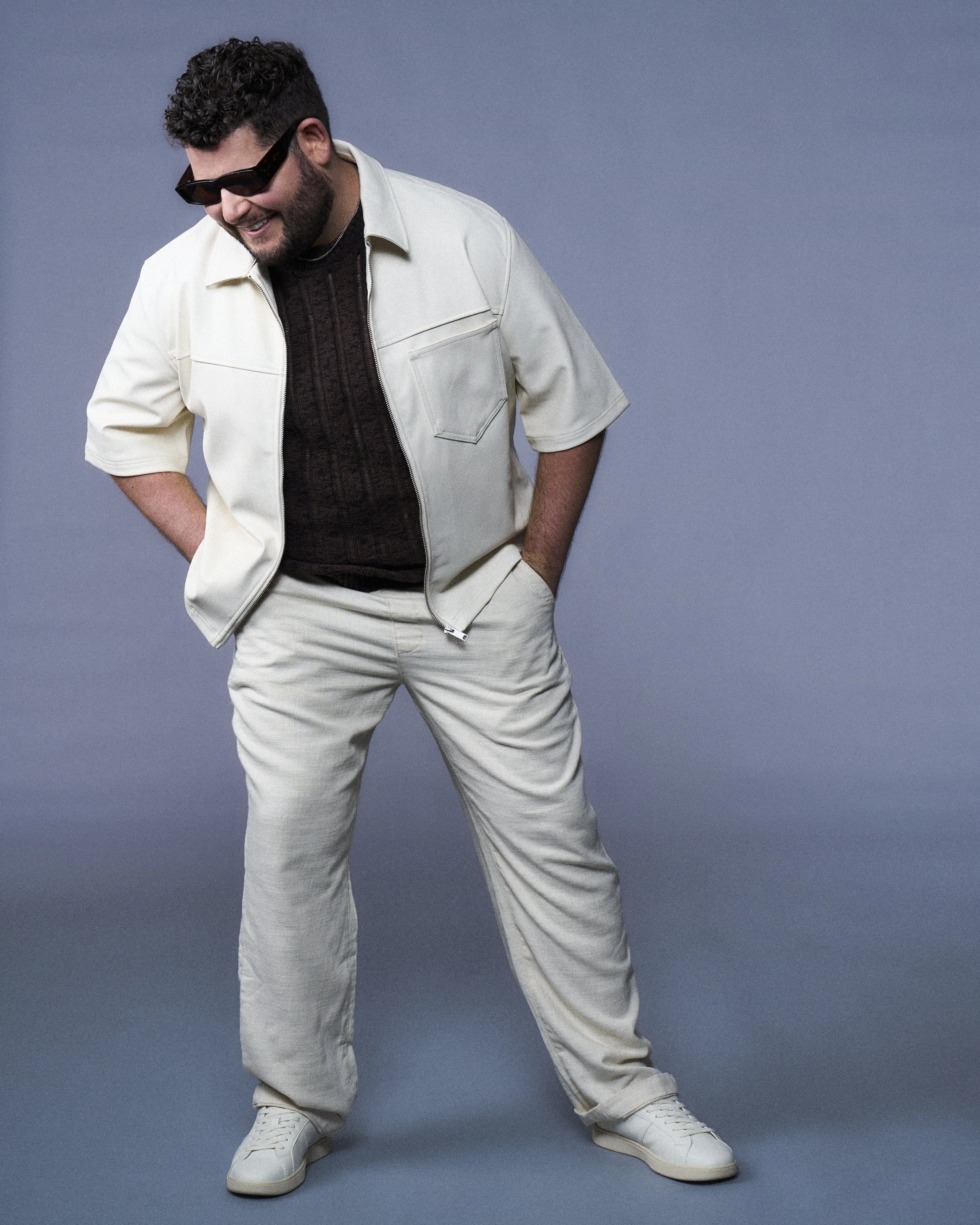 Editorial full-body portrait of actor Nicholas Molencupp smiling in sunglasses and a white casual suit