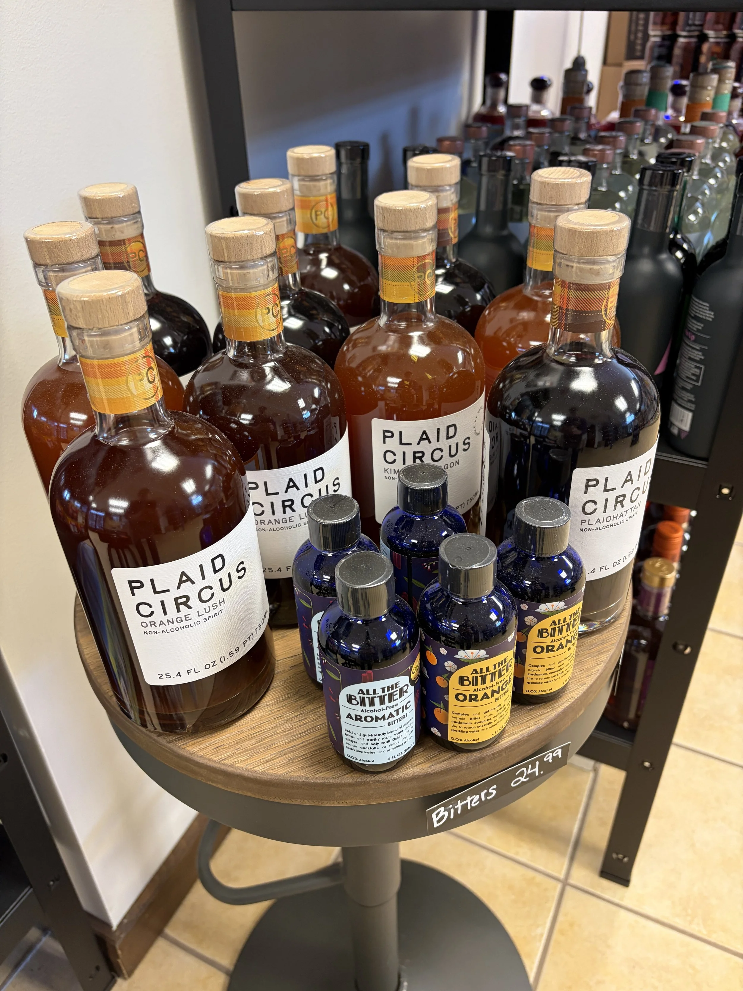 Bottles of non-alcoholic spirits and bitters on a small round table labeled 'Bitters 24.99' in a store.