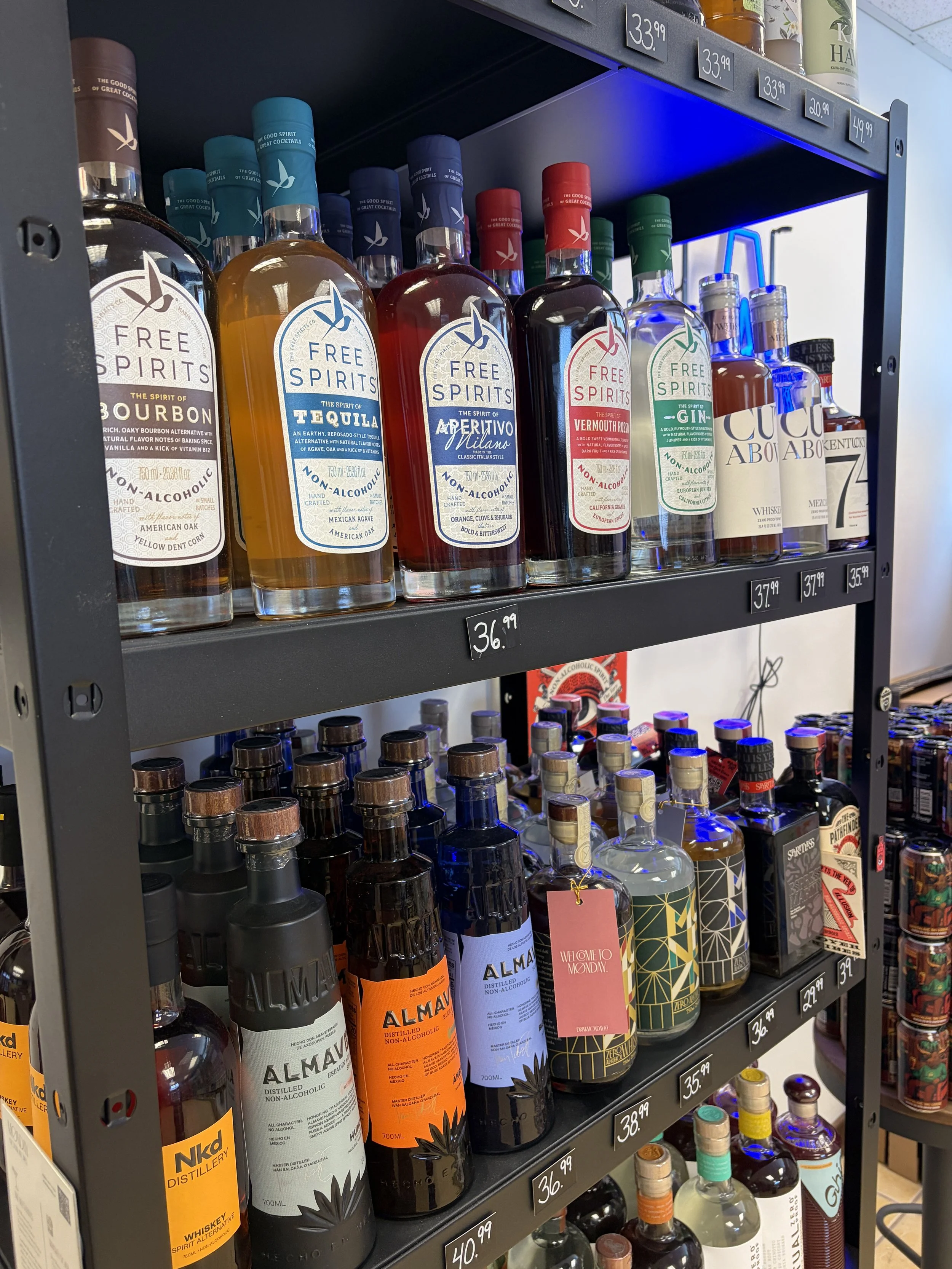Shelf of various non-alcoholic spirits and non-alcoholic bottles, including brands like Free Spirits and Almav, with price tags visible.