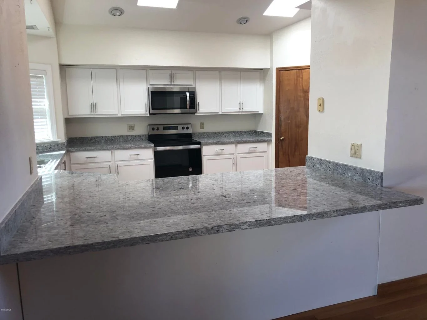 Kitchen with white cabinets, granite countertops, a microwave, oven, and a wooden door.