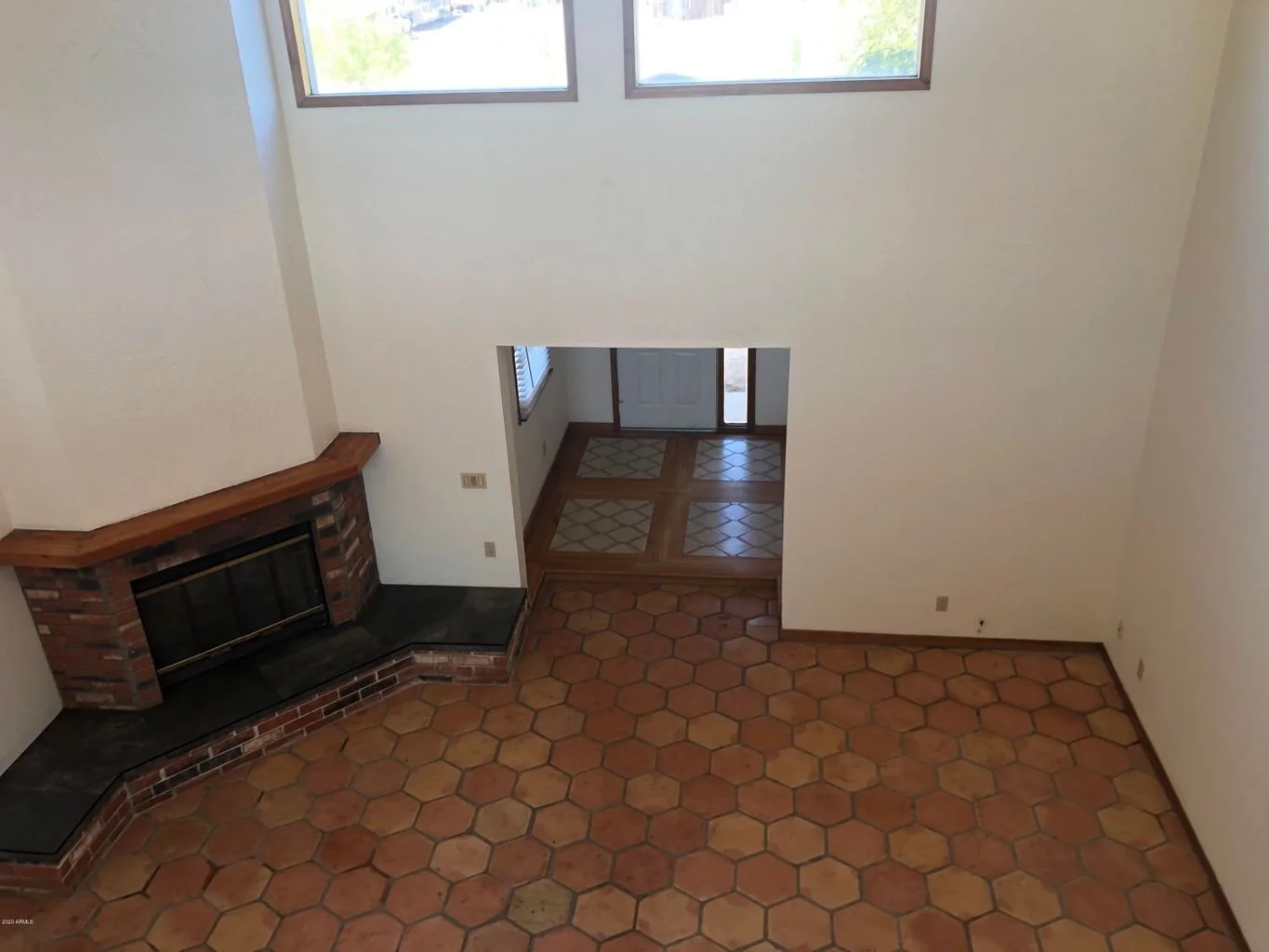 Empty living room with brick fireplace, large windows, and tiled flooring.