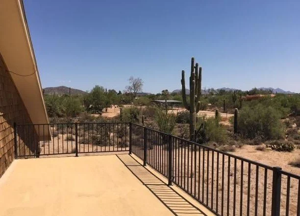 View from a balcony overlooking a desert landscape with a tall cactus and sparse vegetation under a clear blue sky.