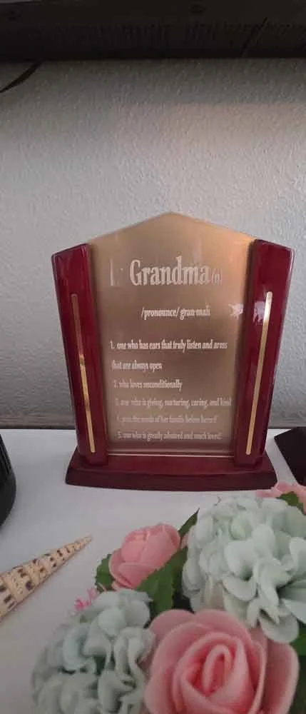 Decorative plaque titled 'Grandma' with an inspirational quote, surrounded by floral arrangements including pink roses and white hydrangeas.
