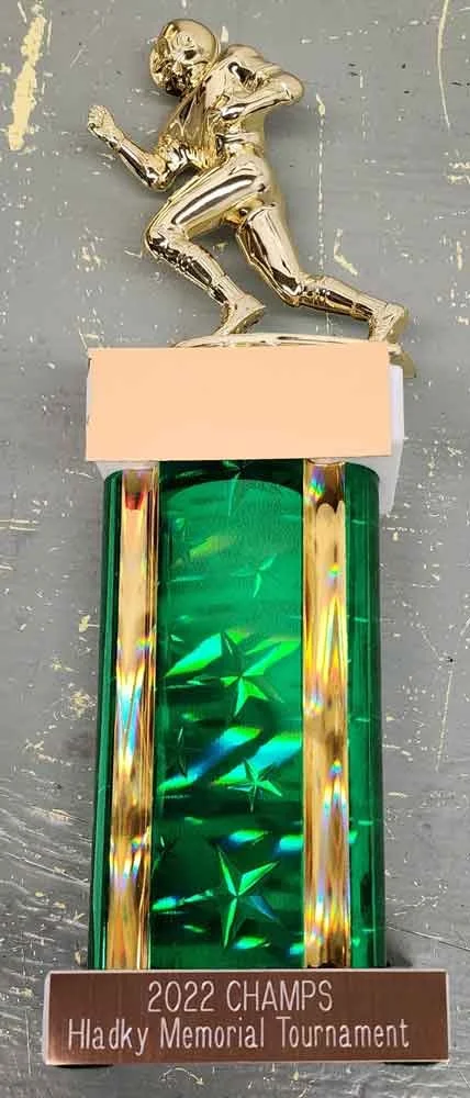 A sports trophy featuring a gold-colored football player figure at the top, a peach-colored platform, a green transparent column with star patterns, and a bronze-colored base with the inscription "2022 CHAMPS Hladky Memorial Tournament."