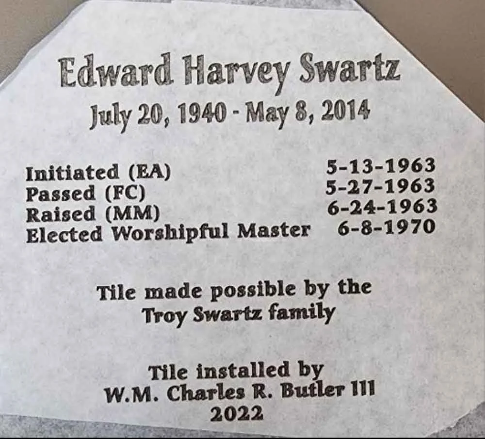 A memorial tile with engraved details about Edward Harvey Swartz, including his birth and death dates, and milestones in his religious life, indicating it was made by the Troy Swartz family and installed by W.M. Charles R. Butler III in 2022.
