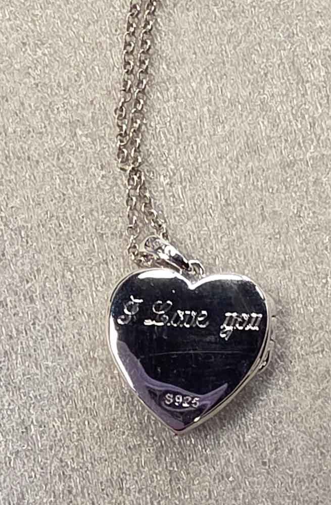 Silver heart-shaped locket hanging from a chain on a light-colored fabric background.